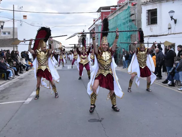 Grupo de personas disfrazadas desfilando con lanzas y trajes históricos por una calle urbana