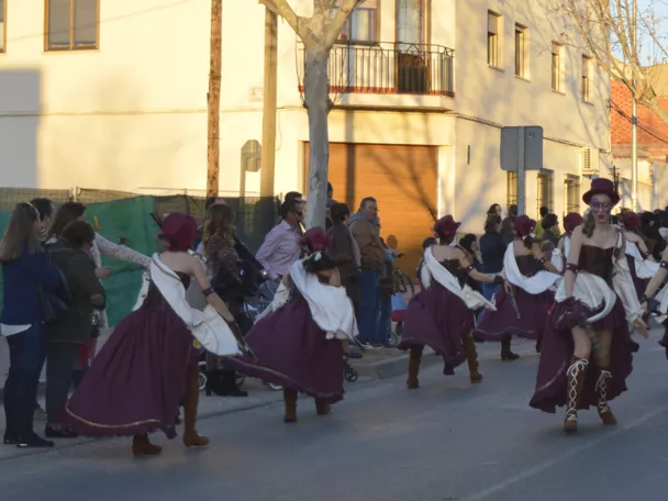 Comparsa con vestuario rojo y dorado avanza en desfile rodeada de público.