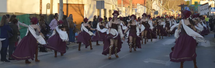 Comparsa con vestuario rojo y dorado avanza en desfile rodeada de público.