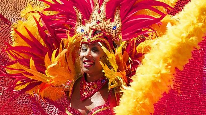 Persona con tocado rojo y amarillo de plumas durante un desfile de carnaval.