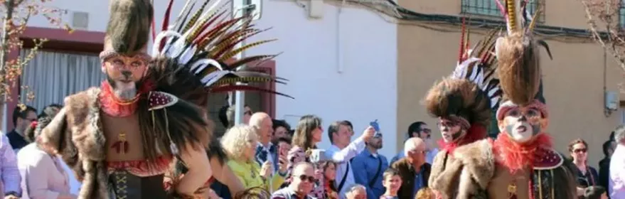 Dos personas con disfraces tribales, plumas altas y faldas rojas desfilando ante el público.