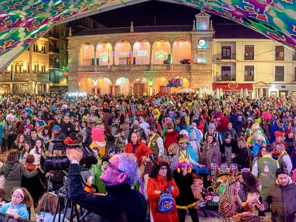 Plaza abarrotada de personas con disfraces bajo carpa iluminada.