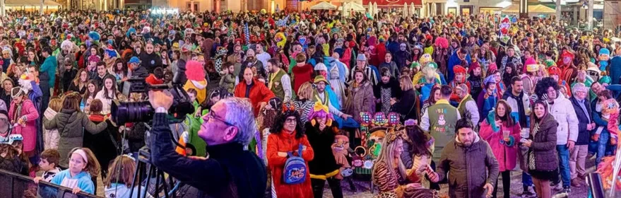 Plaza abarrotada de personas con disfraces bajo carpa iluminada.