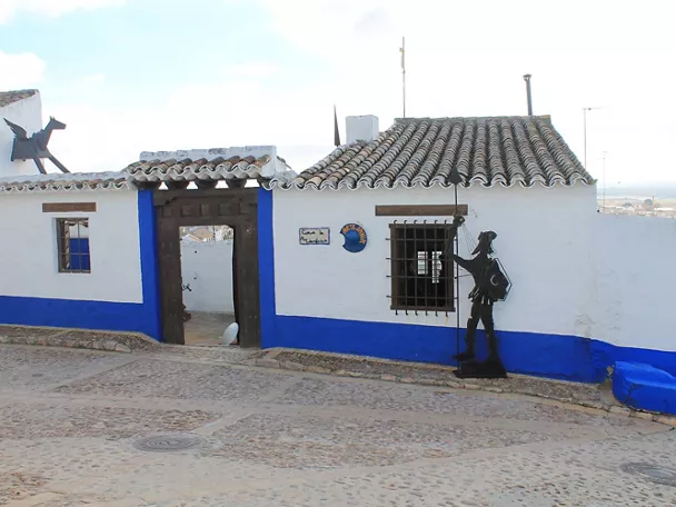 Fachada encalada con zócalo azul y escultura metálica