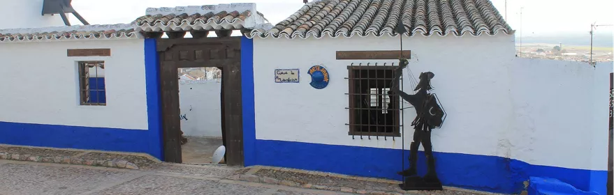 Fachada encalada con zócalo azul y escultura metálica