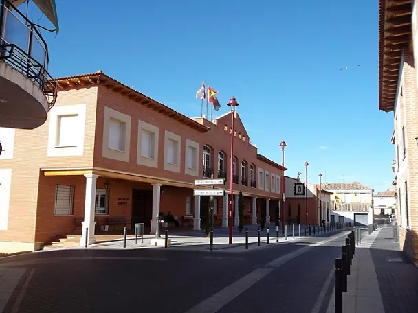 Edificio público de ladrillo con soportales y banderas en una calle tranquila.