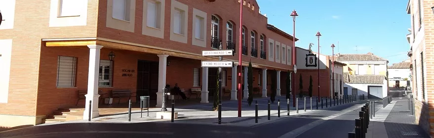 Edificio público de ladrillo con soportales y banderas en una calle tranquila.