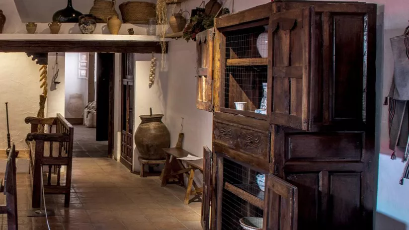 Interior de cocina tradicional con mesa preparada y vasijas de barro.