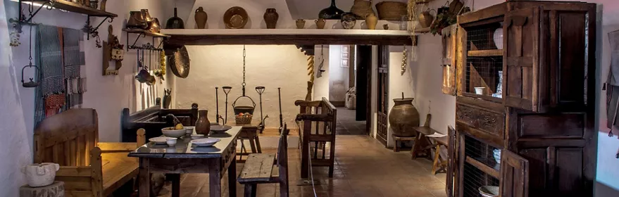 Interior de cocina tradicional con mesa preparada y vasijas de barro.