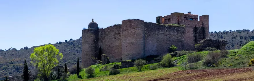 Fortaleza de piedra sobre colina con campos verdes