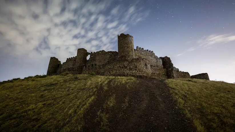 Ruinas de fortaleza medieval bajo cielo nocturno estrellado