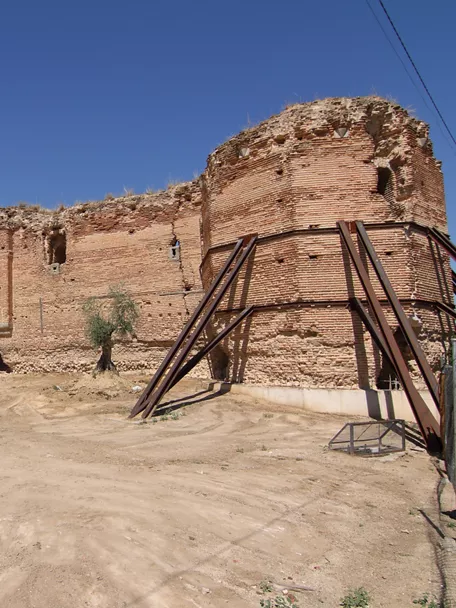 Muralla y torre de ladrillo con arco de acceso en una fortificación en ruinas, reforzada con estructuras metálicas.