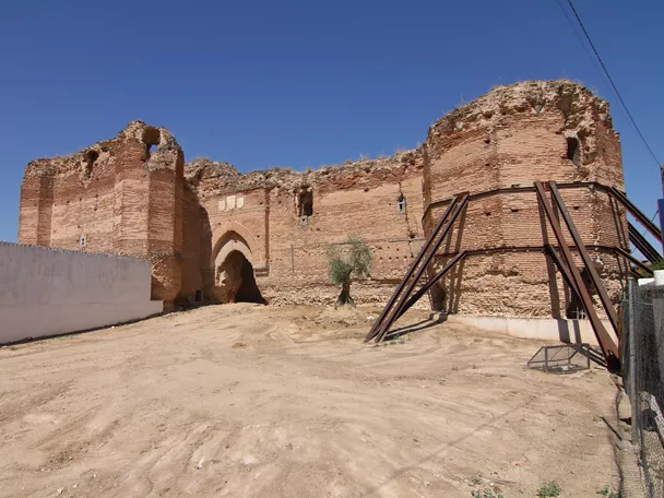 Muralla y torre de ladrillo con arco de acceso en una fortificación en ruinas, reforzada con estructuras metálicas.