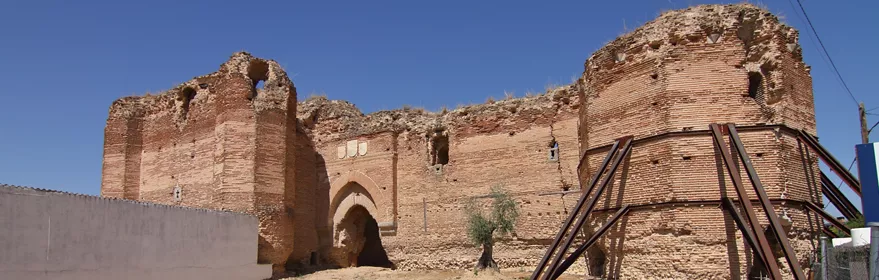 Muralla y torre de ladrillo con arco de acceso en una fortificación en ruinas, reforzada con estructuras metálicas.
