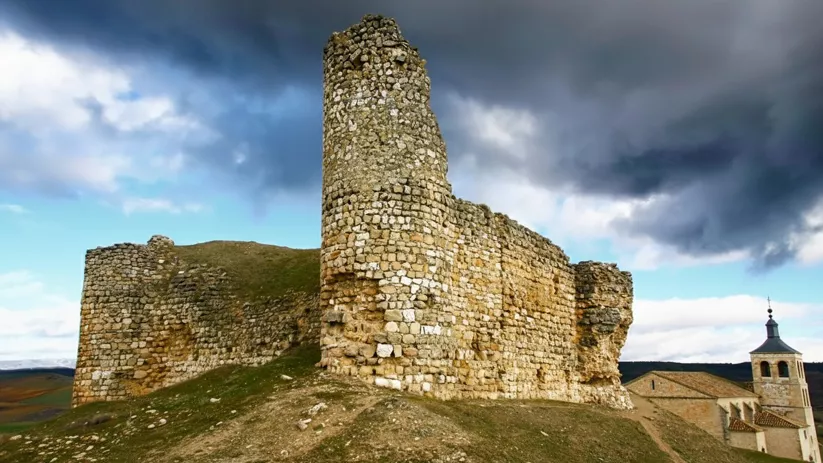 Restos de muralla y torre sobre paisaje abierto.
