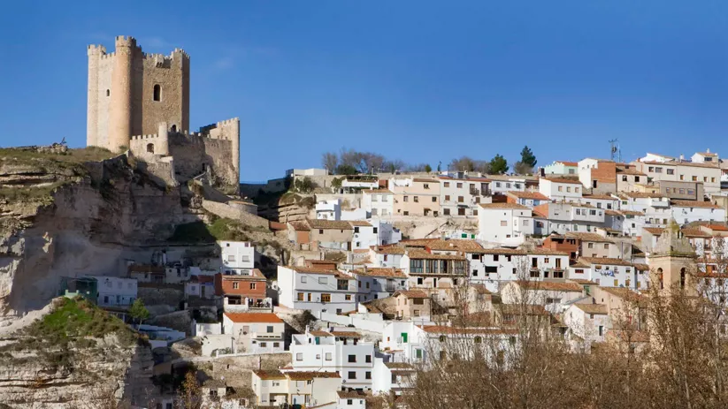 Vista panorámica de un pueblo blanco escalonado bajo una fortaleza en lo alto del cerro.