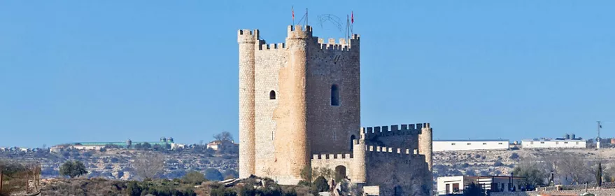 Vista frontal de una fortaleza de piedra con torres almenadas sobre un terreno seco.
