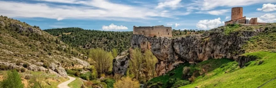 Camino rural y puente de piedra bajo un castillo en lo alto del acantilado.