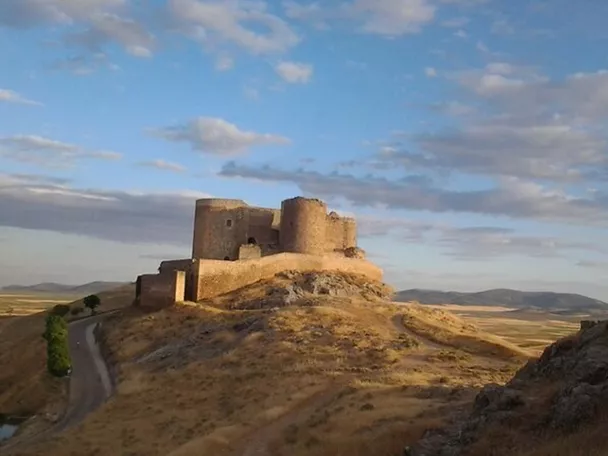Fortaleza de piedra sobre una colina rodeada de campos al atardecer.
