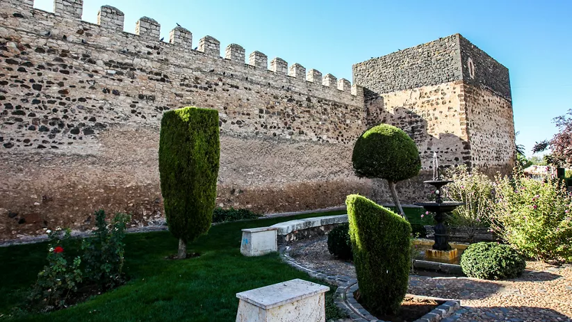 Muralla de piedra con torre y jardín interior del castillo.