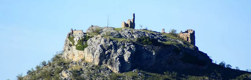 Ruinas de una fortificación sobre una colina rocosa con vegetación y cielo despejado.