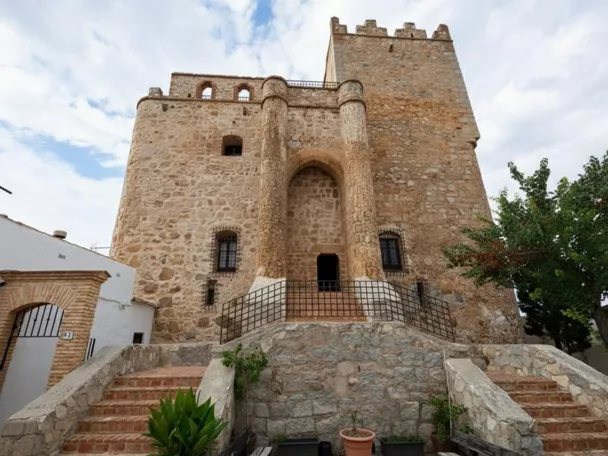Construcción fortificada con muros gruesos, almenas y escaleras laterales de ladrillo.