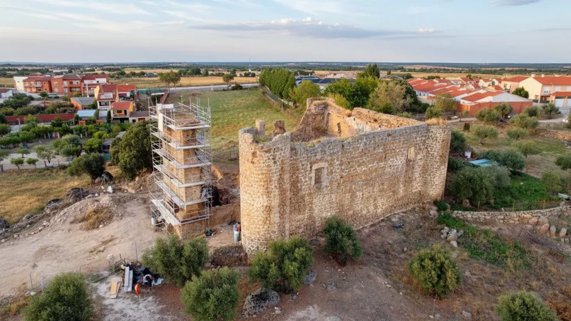 Vista aérea de castillo de piedra en restauración junto a zona residencial y campos abiertos.
