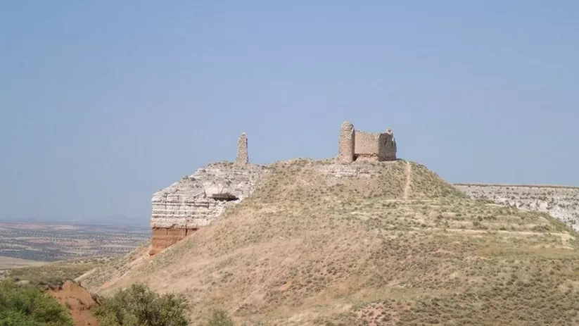 Ruinas de fortaleza sobre colina árida con restos de torres de piedra.