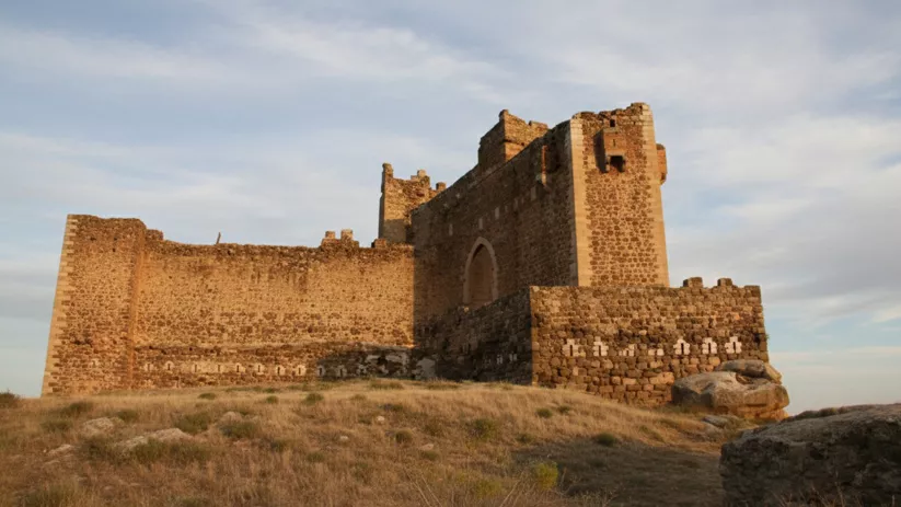 Fachada lateral de castillo con torres y puerta apuntada.