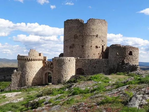 Vista aérea de un castillo rodeado de montes y formaciones rocosas.