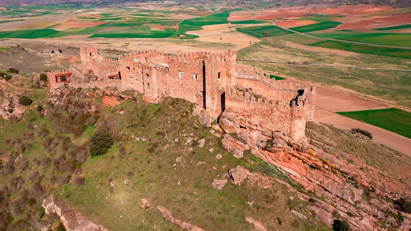 Fortaleza de piedra sobre una colina con campos agrícolas alrededor.