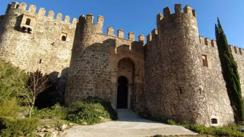 Fachada de fortaleza medieval con torres cilíndricas y muralla almenada de piedra.