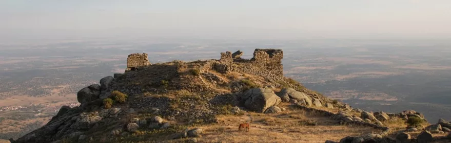 Ruinas de fortaleza en la cima de una montaña al atardecer.