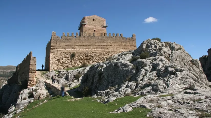 Castillo de piedra sobre peñasco rocoso bajo cielo despejado.