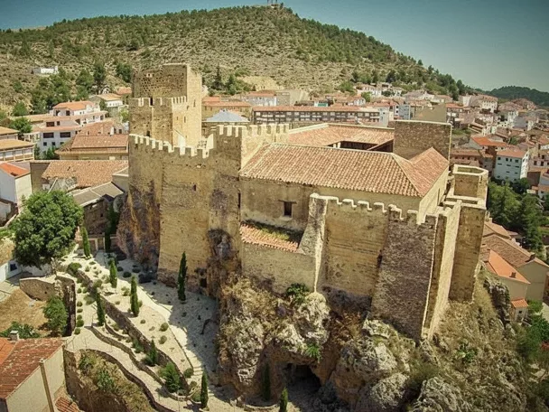 Vista aérea de castillo medieval sobre peñasco junto a un pueblo.