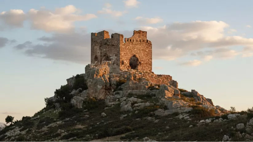 Construcción defensiva en ruinas sobre peñas y matorrales.