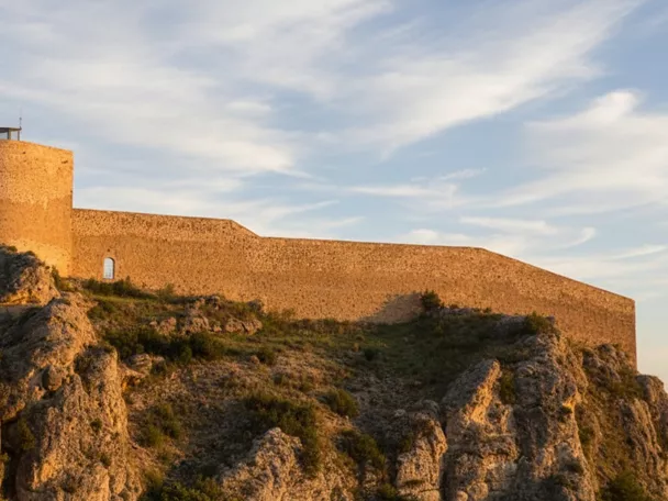 Fortaleza de piedra sobre colina rocosa al atardecer.
