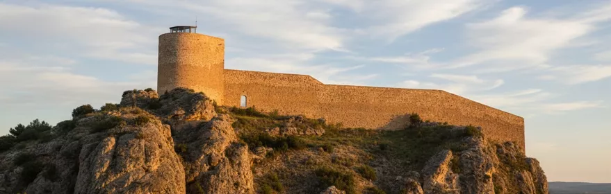 Fortaleza de piedra sobre colina rocosa al atardecer.