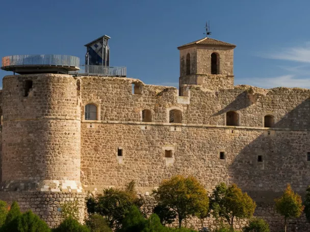Castillo de piedra con torres circulares sobre colina