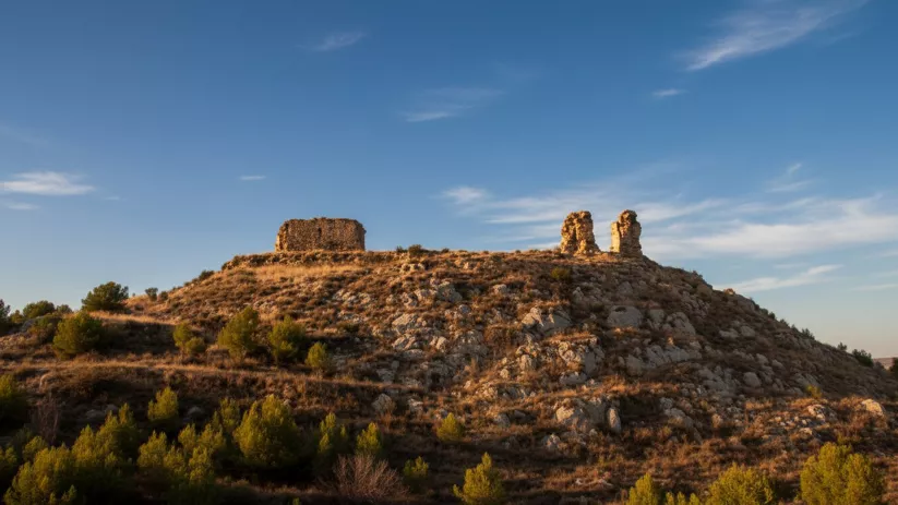 Ruinas de torre sobre loma rocosa al atardecer.