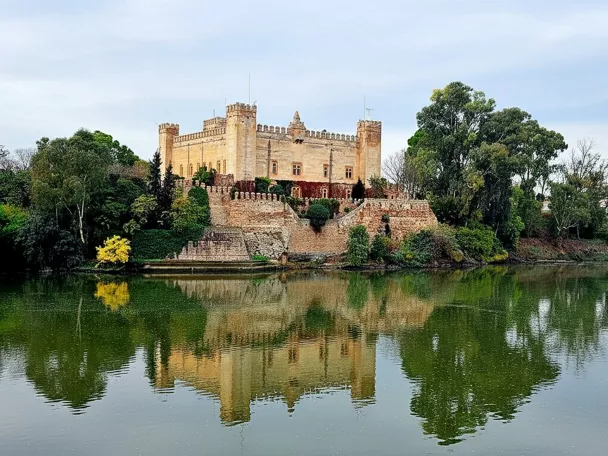 Edificio fortificado de estilo medieval junto al río con murallas y torres cuadradas.
