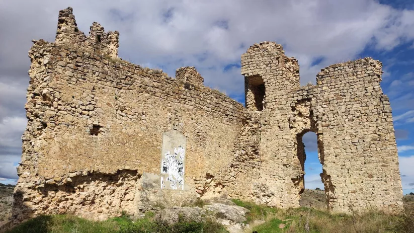 Muro de piedra con torre y arco en ruinas.
