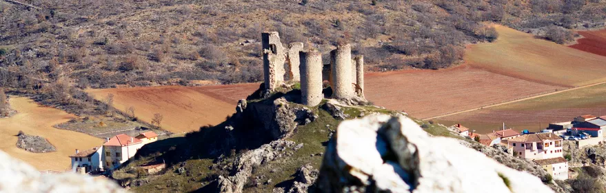 Ruinas de castillo sobre colina rodeada de campos.