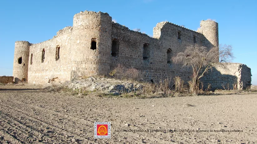 Castillo de piedra parcialmente derruido en paisaje árido con cielo despejado.