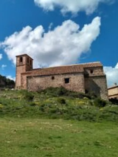 Iglesia de piedra sobre una colina verde bajo cielo azul con nubes.