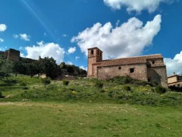 Iglesia de piedra sobre una colina verde bajo cielo azul con nubes.