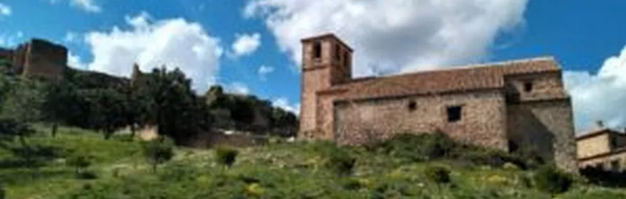 Iglesia de piedra sobre una colina verde bajo cielo azul con nubes.