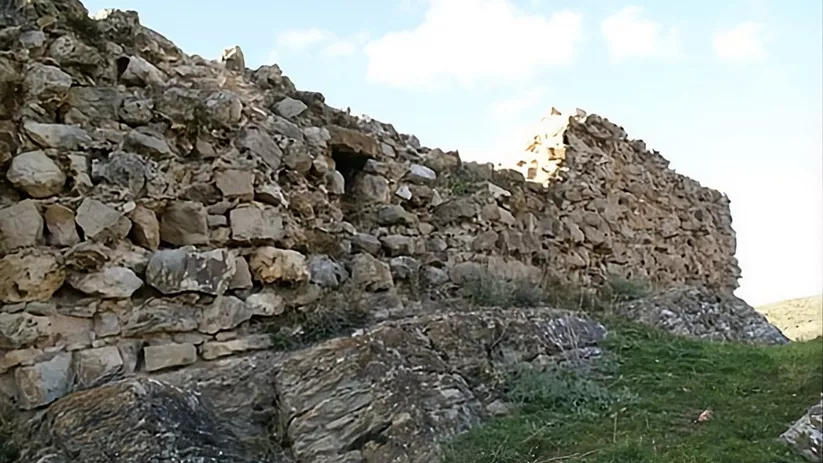 Restos de muralla de piedra sobre ladera verde.