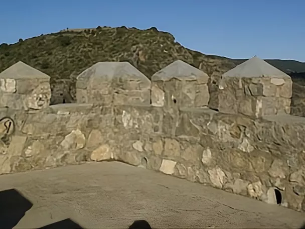Muralla con almenas y paisaje montañoso al fondo.