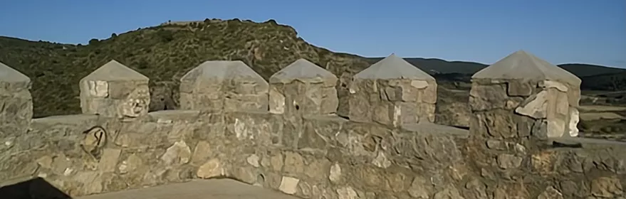 Muralla con almenas y paisaje montañoso al fondo.